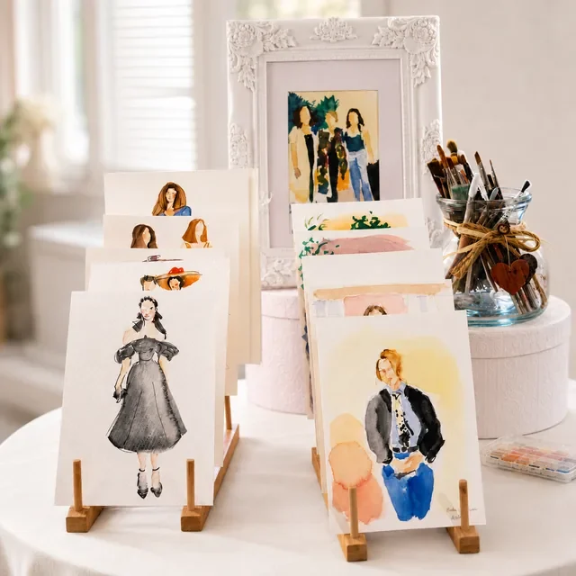 Acuarelas para invitados de boda expuestas en soportes de madera junto a pinceles